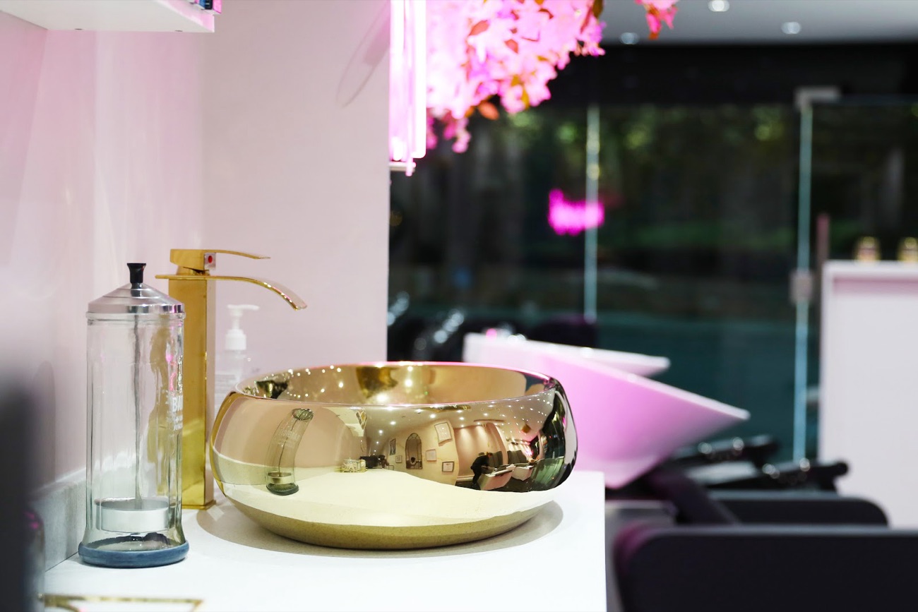 A gold wash basin under pink neon blossom by the window at MyBeautyHub